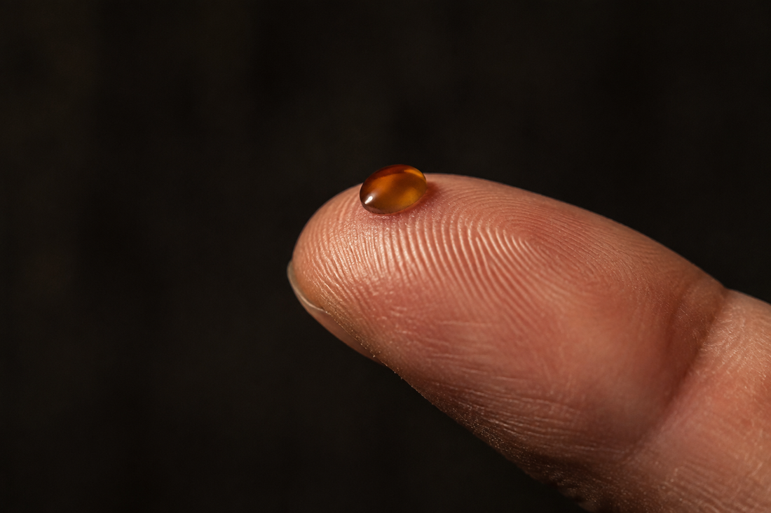 A single amber oil droplet on a fingertip against a dark background
