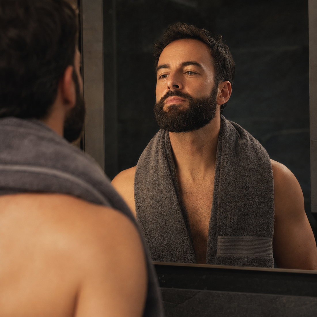 Man with a well-groomed full beard looking into a bathroom mirror after grooming
